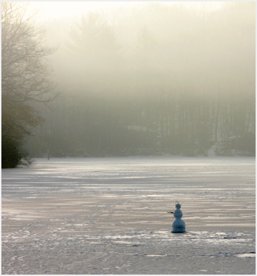 Snowman on frozen lake ice in mist.